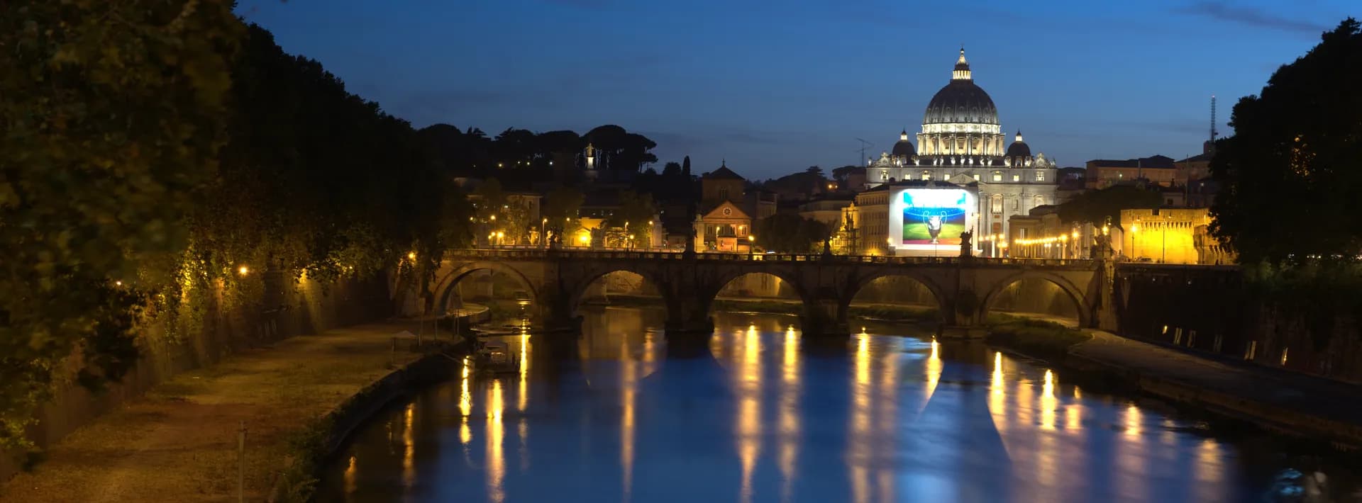 the St. Peter's Basilica seen at night from across the Tiber River in Rome