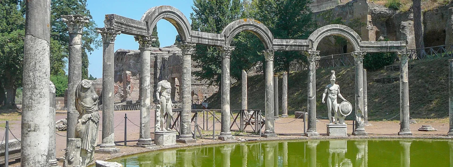 a pool of water surrounded by ruins of Roman statues at Villa Adriana in Tivoli, Italy