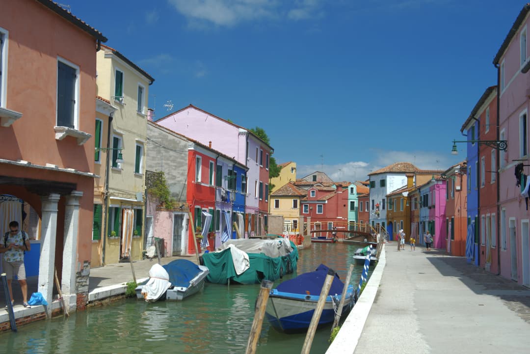 View of canal with anchored boats and colorful buildings in Burano, Italy