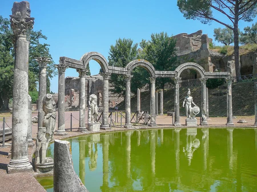 a pool of water surrounded by ruins of Roman statues at Villa Adriana in Tivoli, Italy