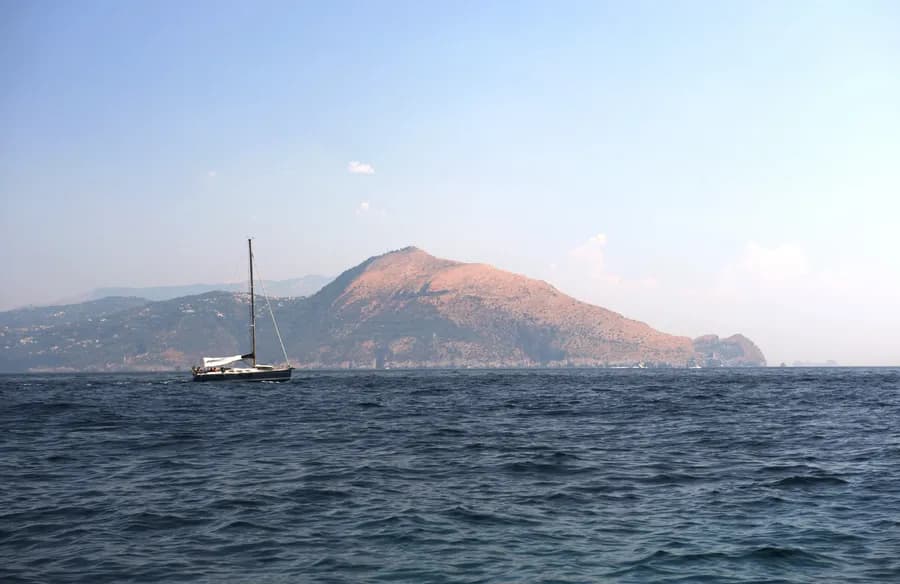 view from the water of a mountain with sailboat in foreground in Capri, Italy